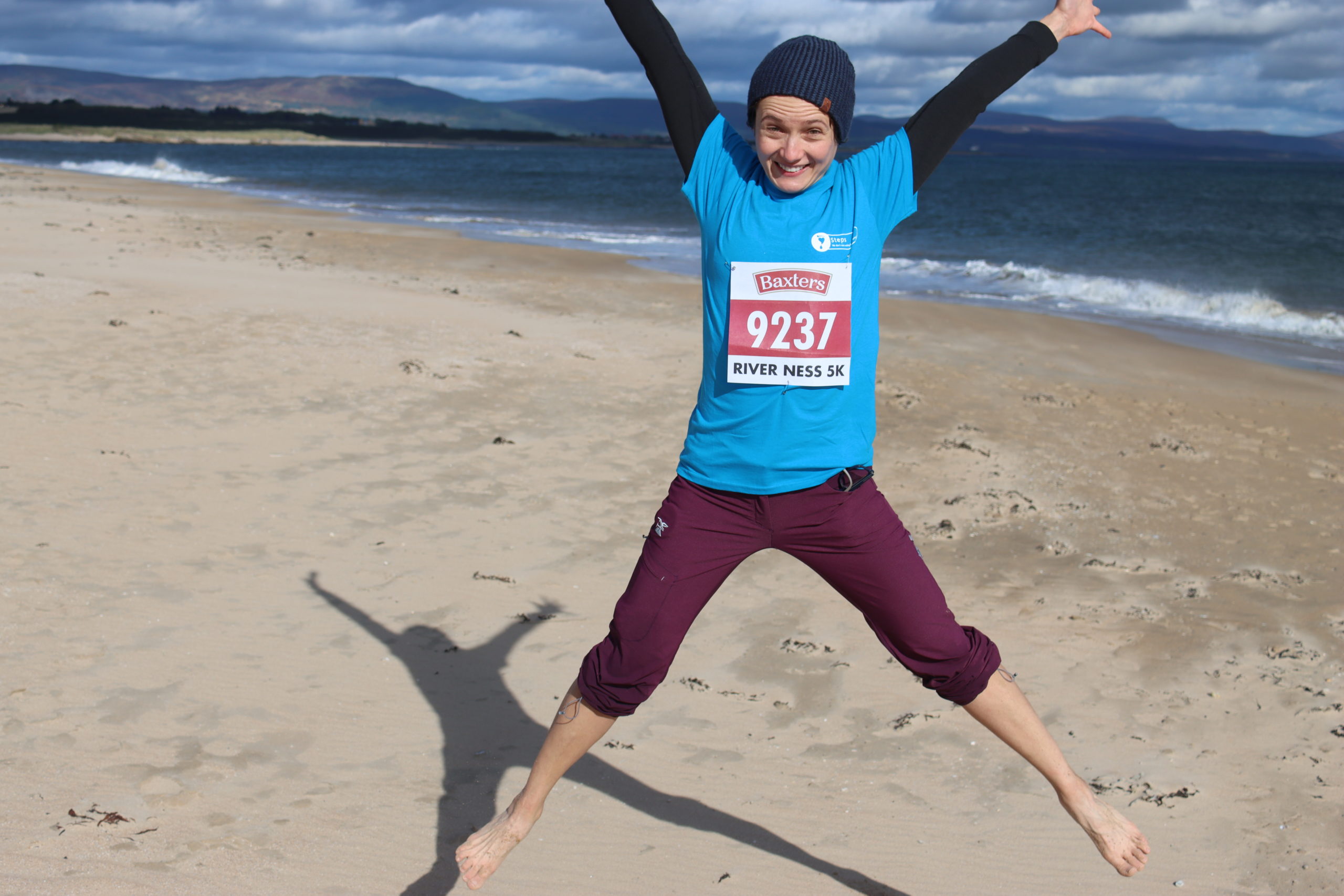 Aggie jumping on the beach in Steps t-shirt